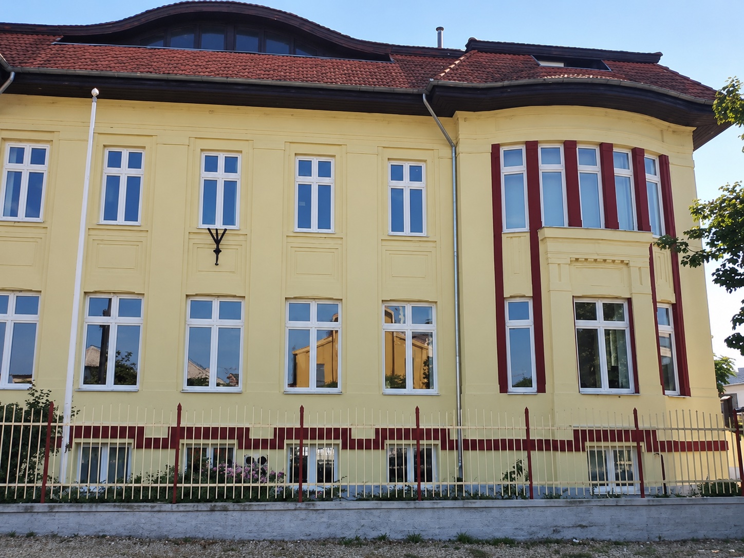 Sárga, bordó pilaszteres homlokzatú kétszintes épület a Hengermalomnál, fehér osztott ablakokkal.
