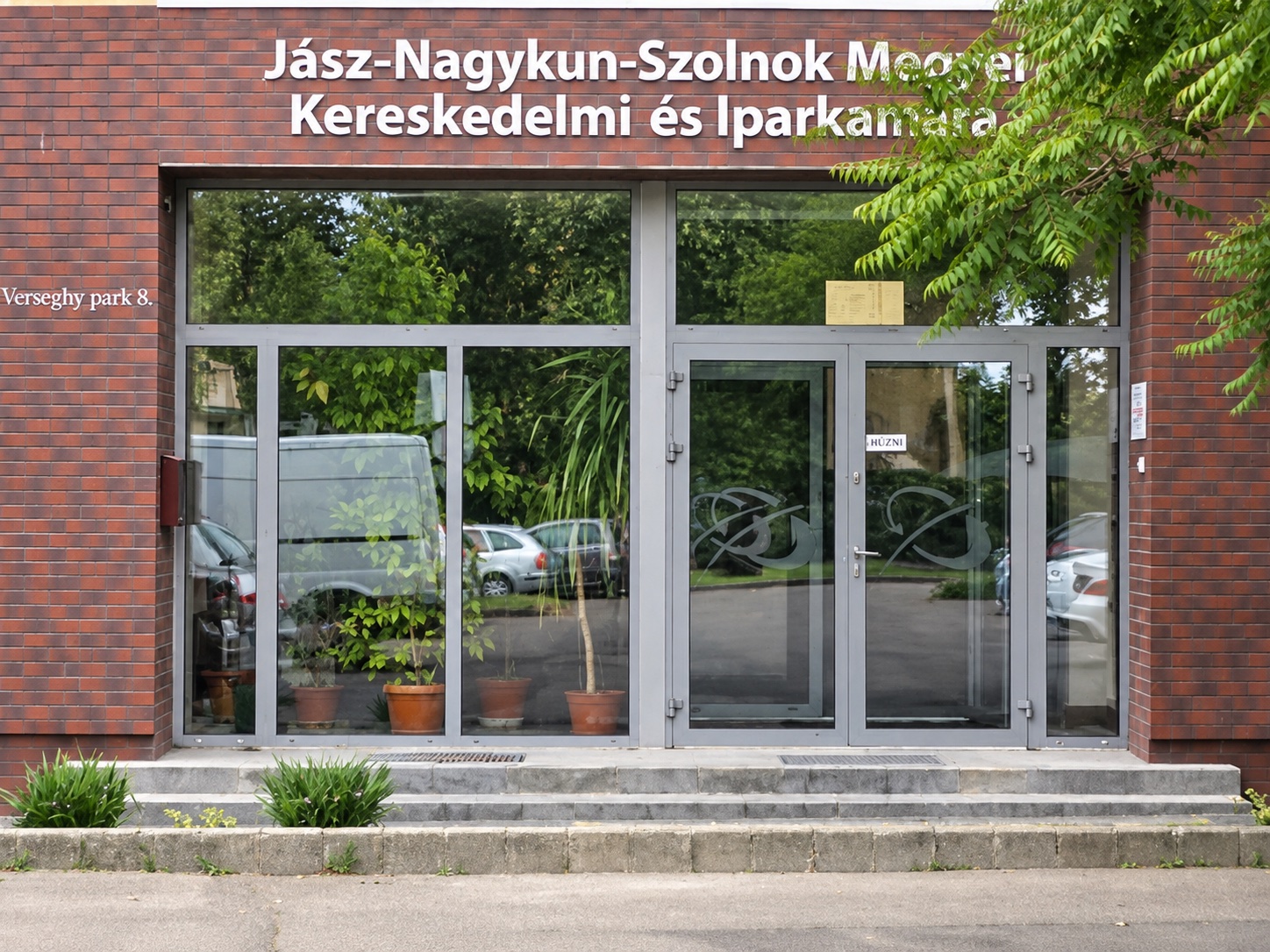 A Jász-Nagykun-Szolnok Megyei Kereskedelmi és Iparkamara téglahomlokzatú bejárata, üvegezett ajtókkal és portállal.